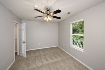 an empty bedroom with a ceiling fan and a window